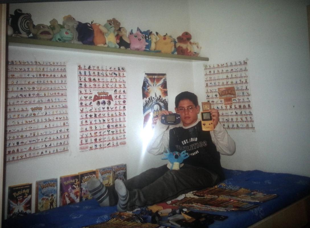 Adrià in his bedroom holding his Game Boy Advance, Game Boy Color, and Pokémon Gold. He is surrounded by Pokémon magazines, videos, posters and plushies (2002)